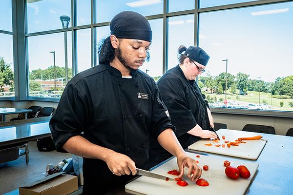 Culinary students chopping vegetables on cutting boards