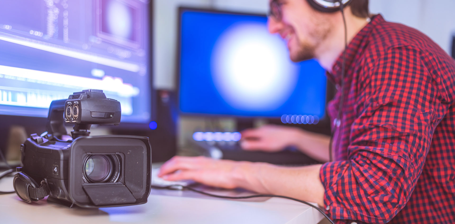 Man editing film on computer in background with digital camera in forefront