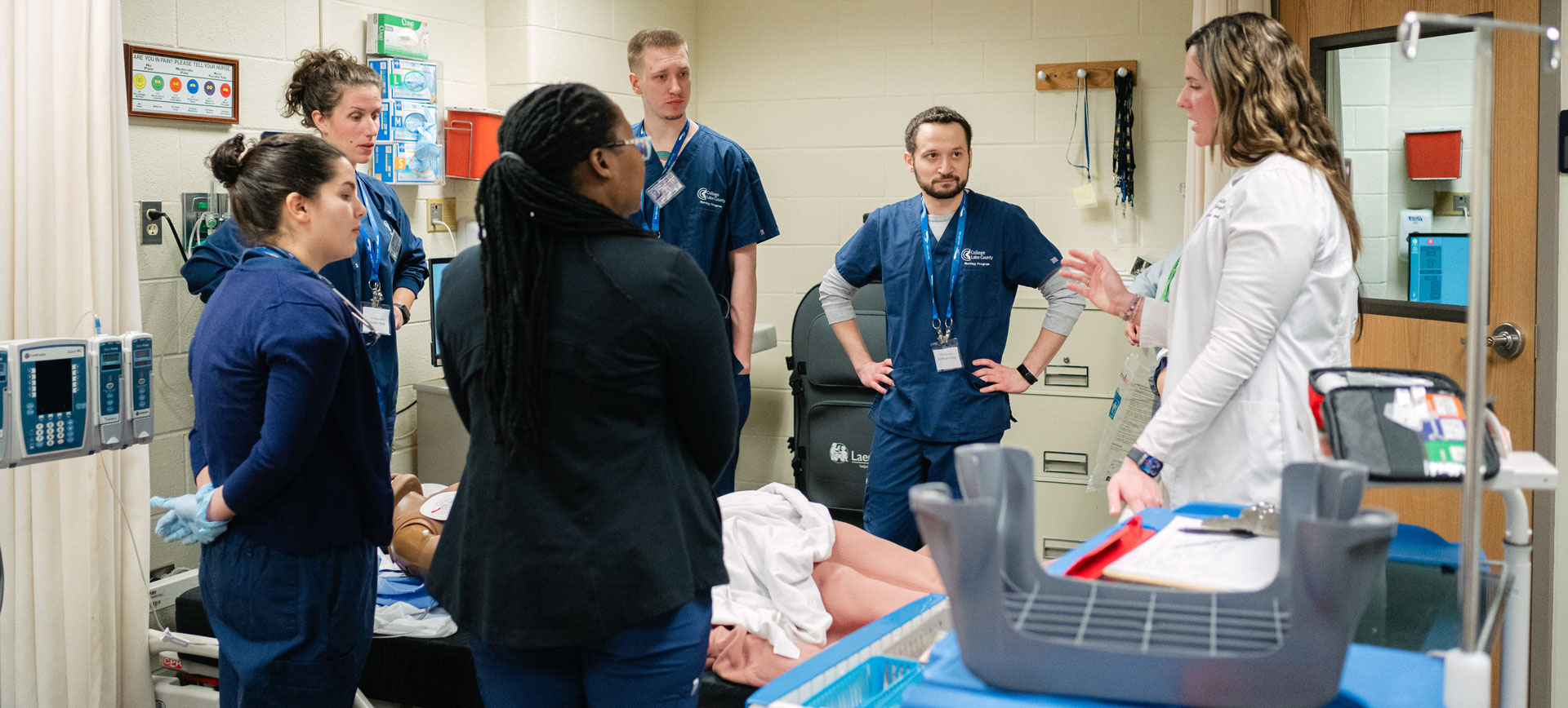 CLC students gathered around hospital dummy listening to an important concept from their instructor