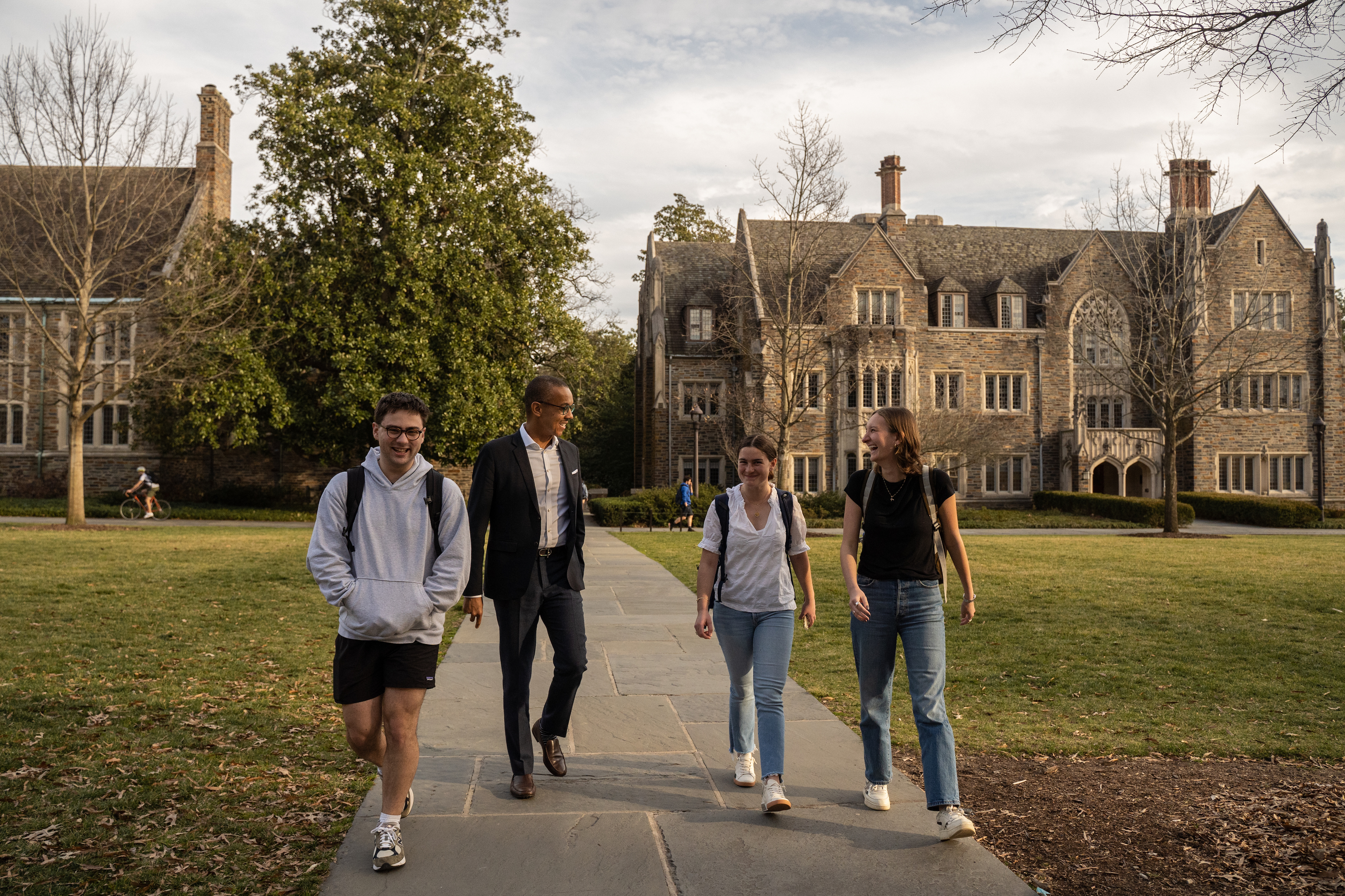 Dean Gary Bennett walks across Abele Quad while talking with three students.