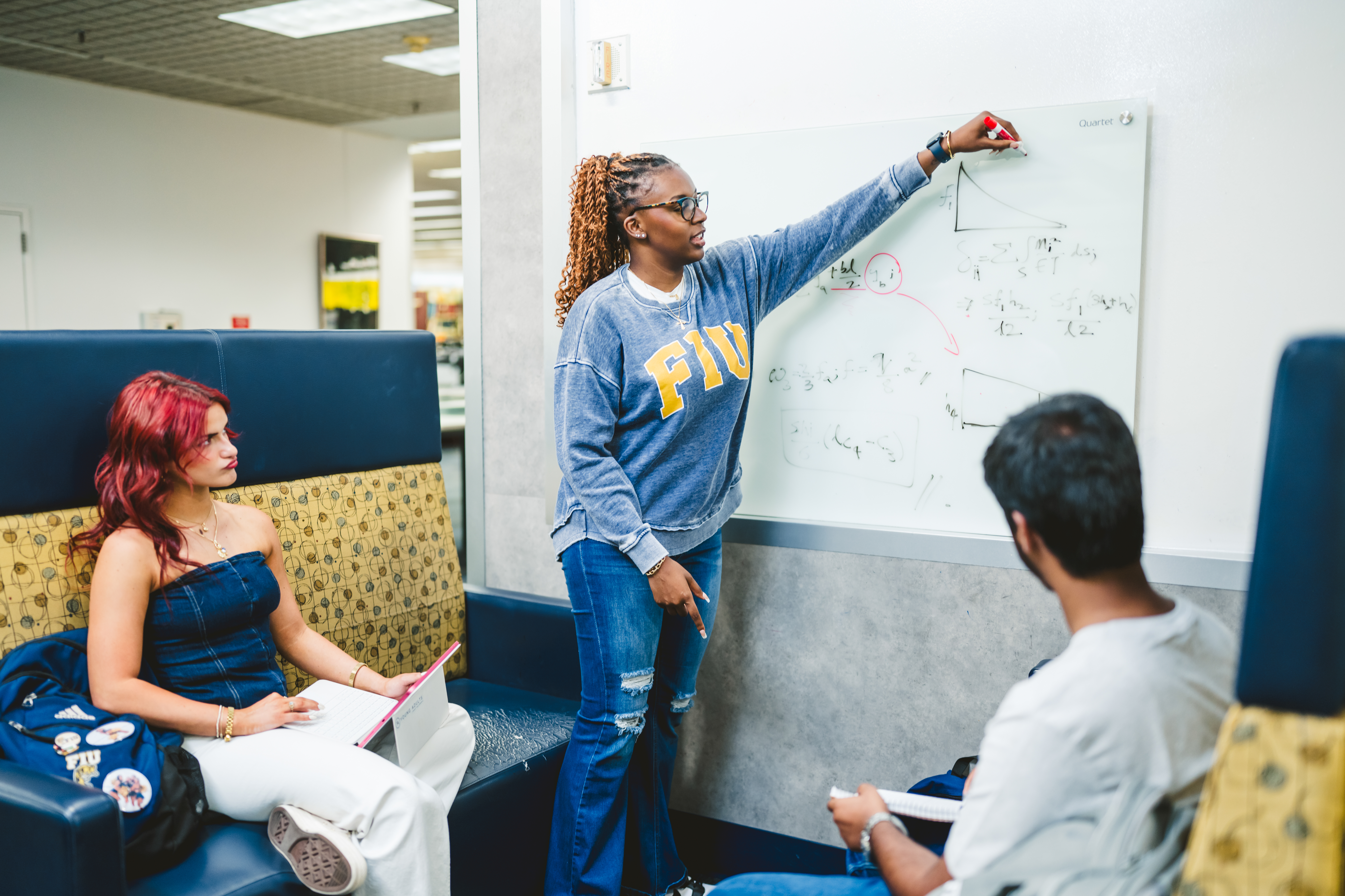 Student study group in Steven and Dorthea Green Library. One student writing on white board while explaining to others.