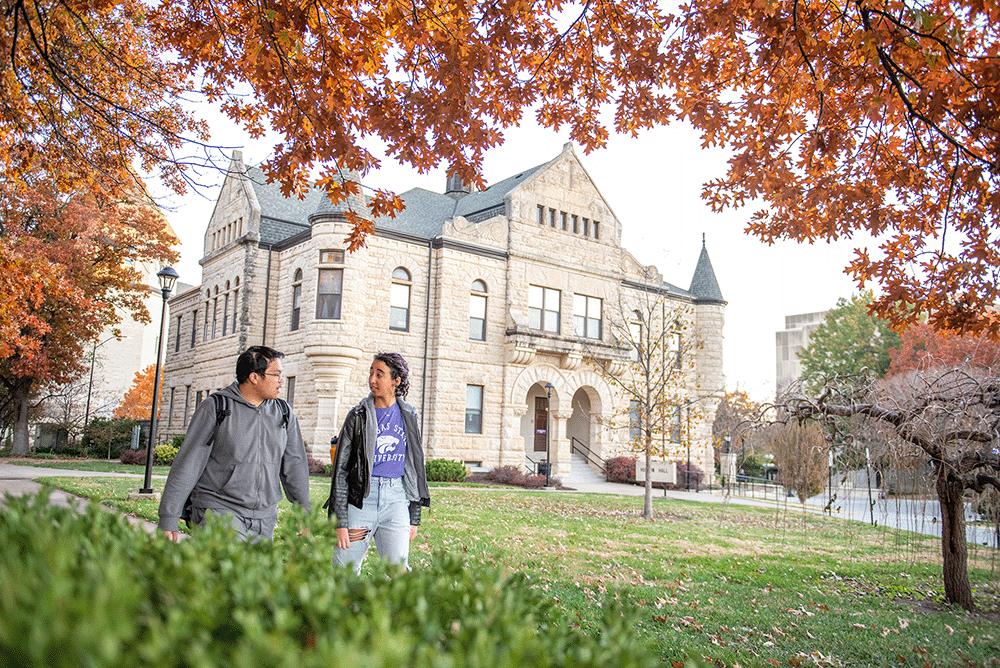 2 students walking with a limestone building in the background