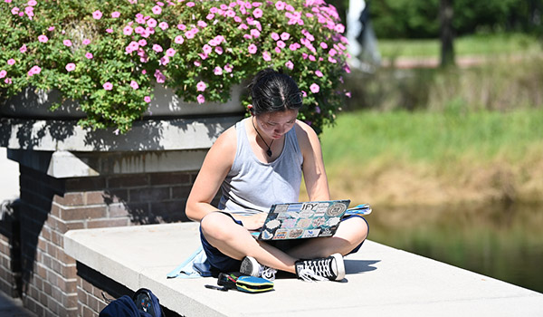 Female student sitting outside on large ledge looking at book